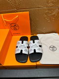 Hermes slide sandals with black footbed and white logo strap across the toe