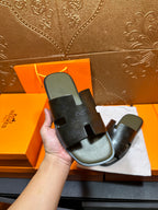 Black slide sandals held in hand, wide straps with embossed logo
