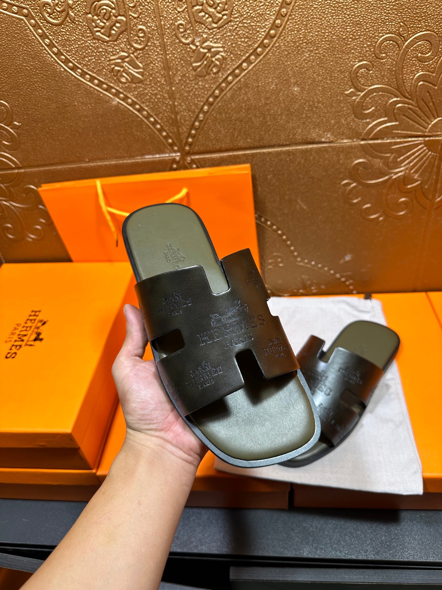 Black slide sandals held in hand, wide straps with embossed logo