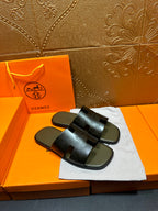 Black slide sandals with wide cutout straps, displayed on white cloth