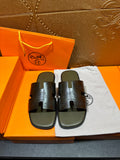 Black slide sandals with textured H cutout straps, on white dust bag
