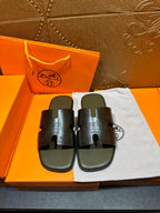 Black slide sandals with textured H cutout straps, on white dust bag