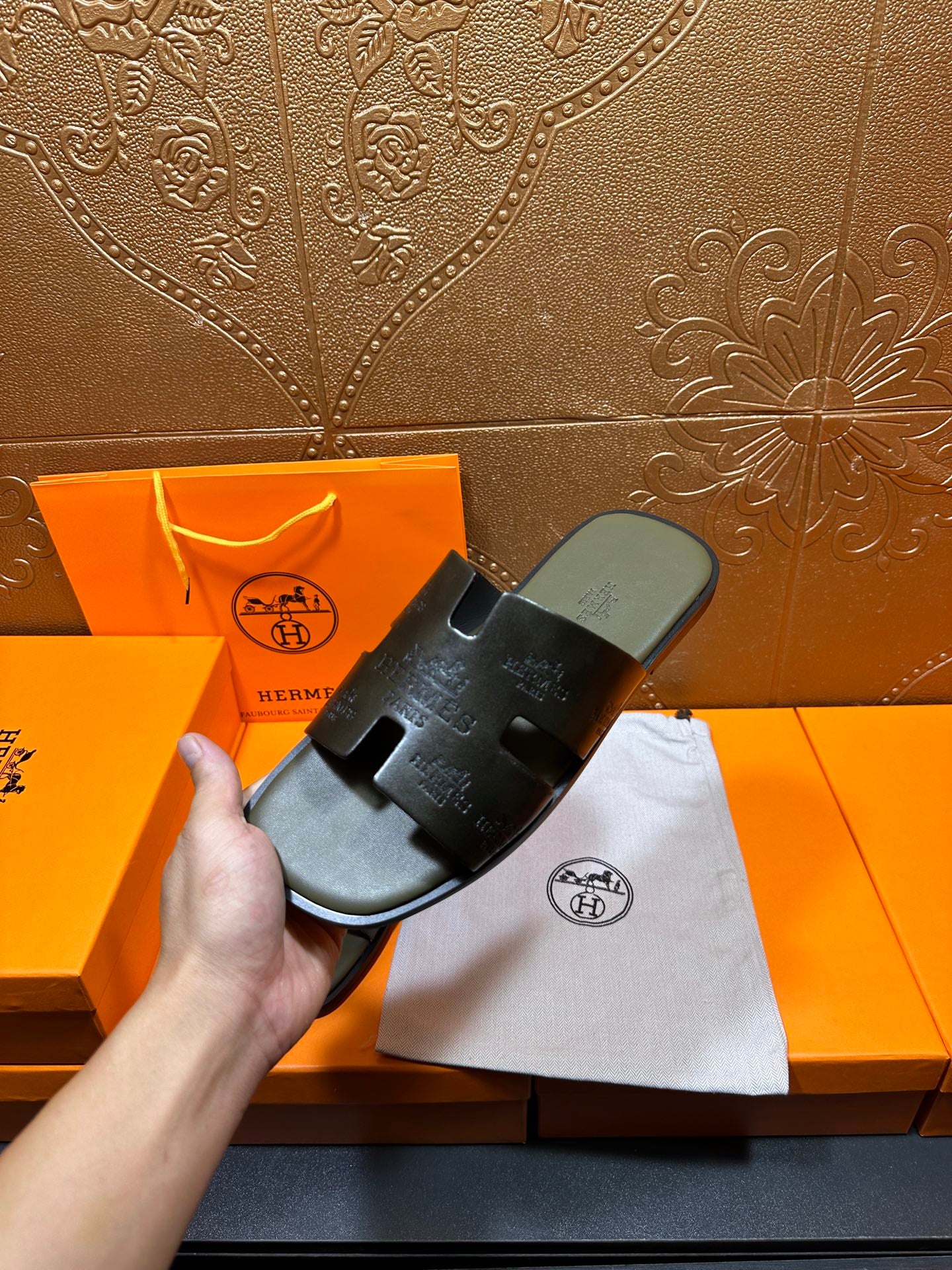 Black slide sandals held in hand over dust bag