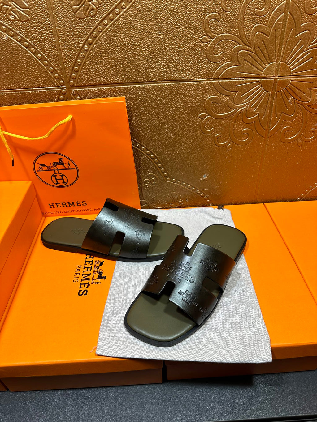Black slide sandals with embossed straps and open toe, on dust bag
