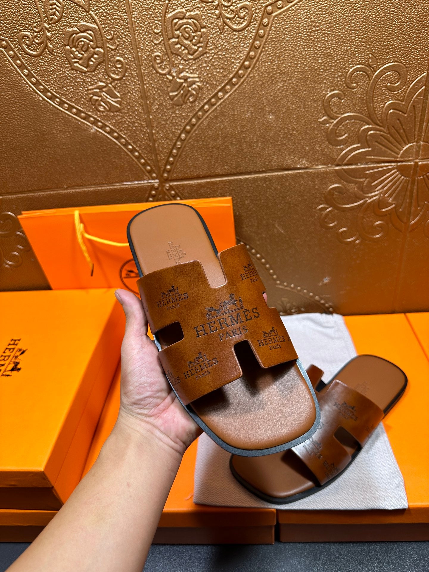 Hermes leather slide sandals held in hand, dark brown with wide strap and logo