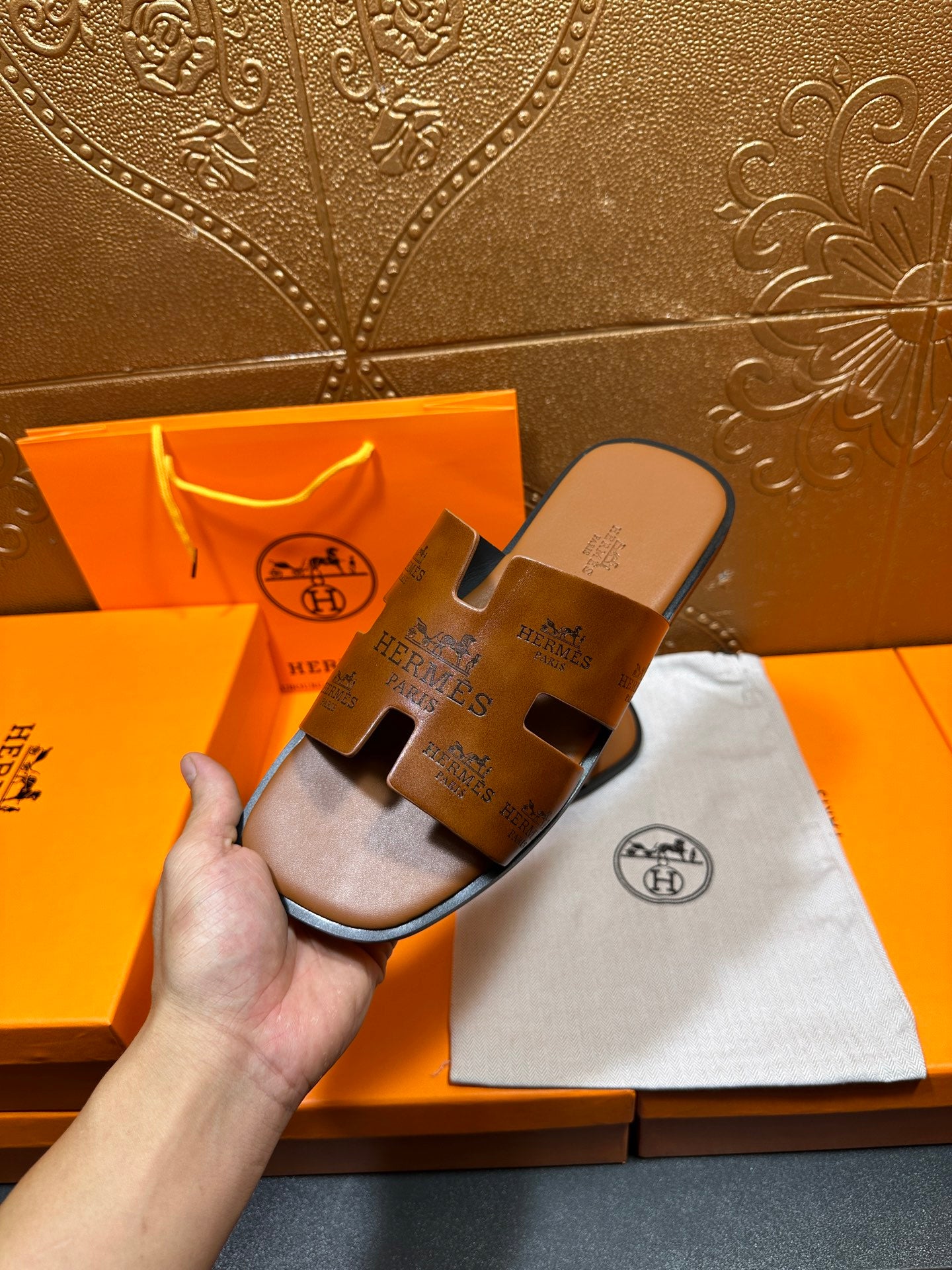 Hermes leather slide sandals held in hand, dark brown slides with logo on straps