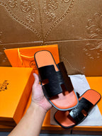 Hermes slide sandals held in hand, black embossed straps with orange footbed