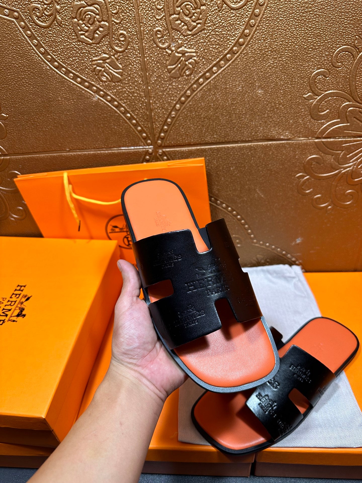 Hermes slide sandals held in hand, black embossed straps with orange footbed