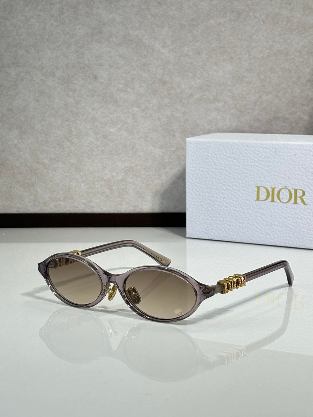Black oval sunglasses with gold hinge logo and light brown lenses