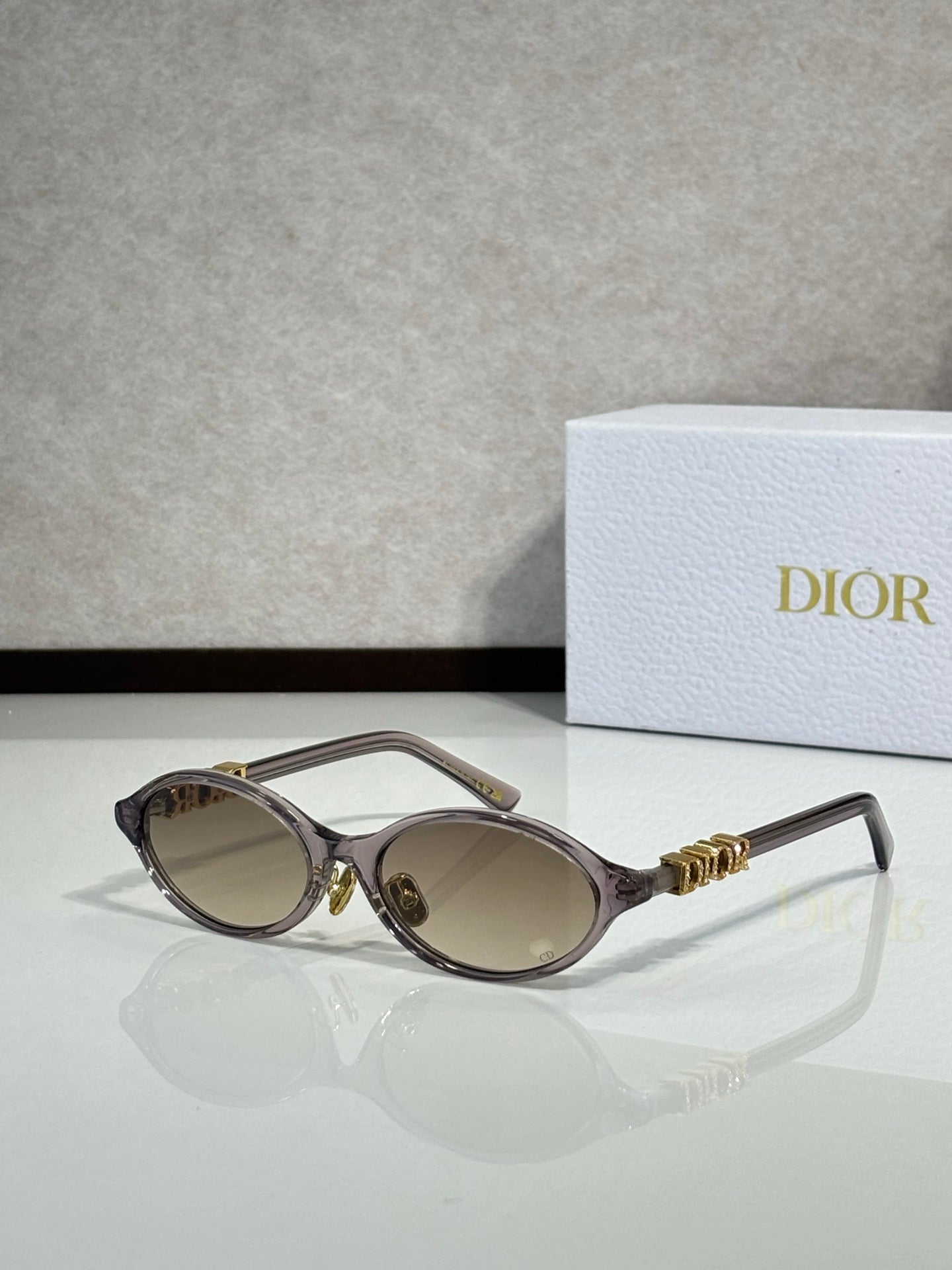 Black oval sunglasses with gold hinge logo and light brown lenses