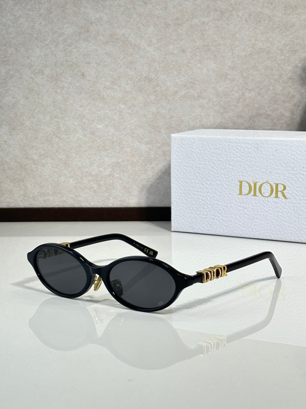 Black oval sunglasses with gold hinge logo and dark lenses