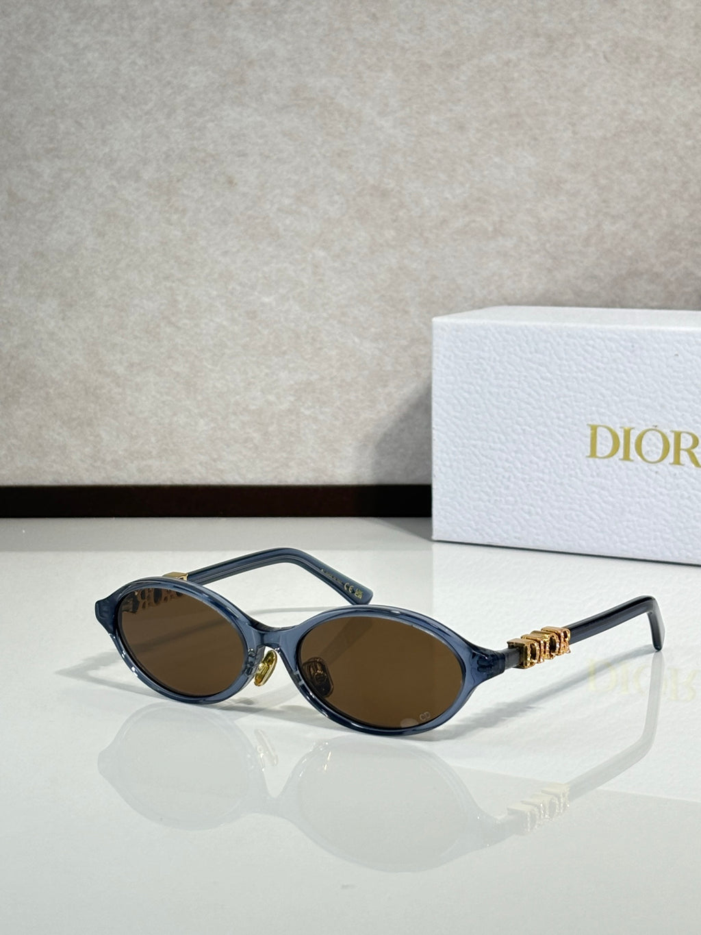 Black oval sunglasses with gold hinge logo and brown-tinted lenses