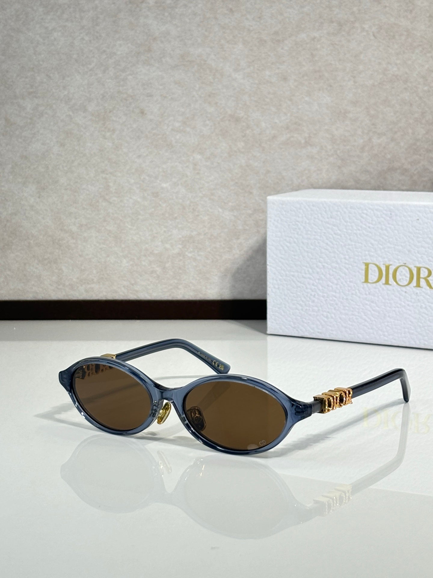 Black oval sunglasses with gold hinge logo and brown-tinted lenses