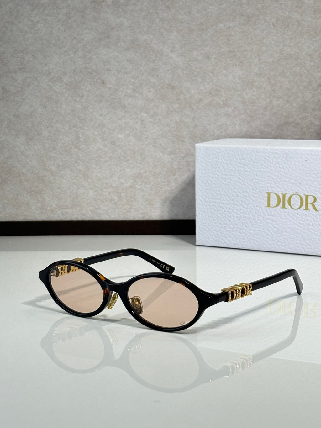 Black oval sunglasses with gold hinge logo and light brown lenses