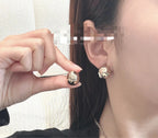 Gold-tone Chanel-style button stud earrings worn with black top