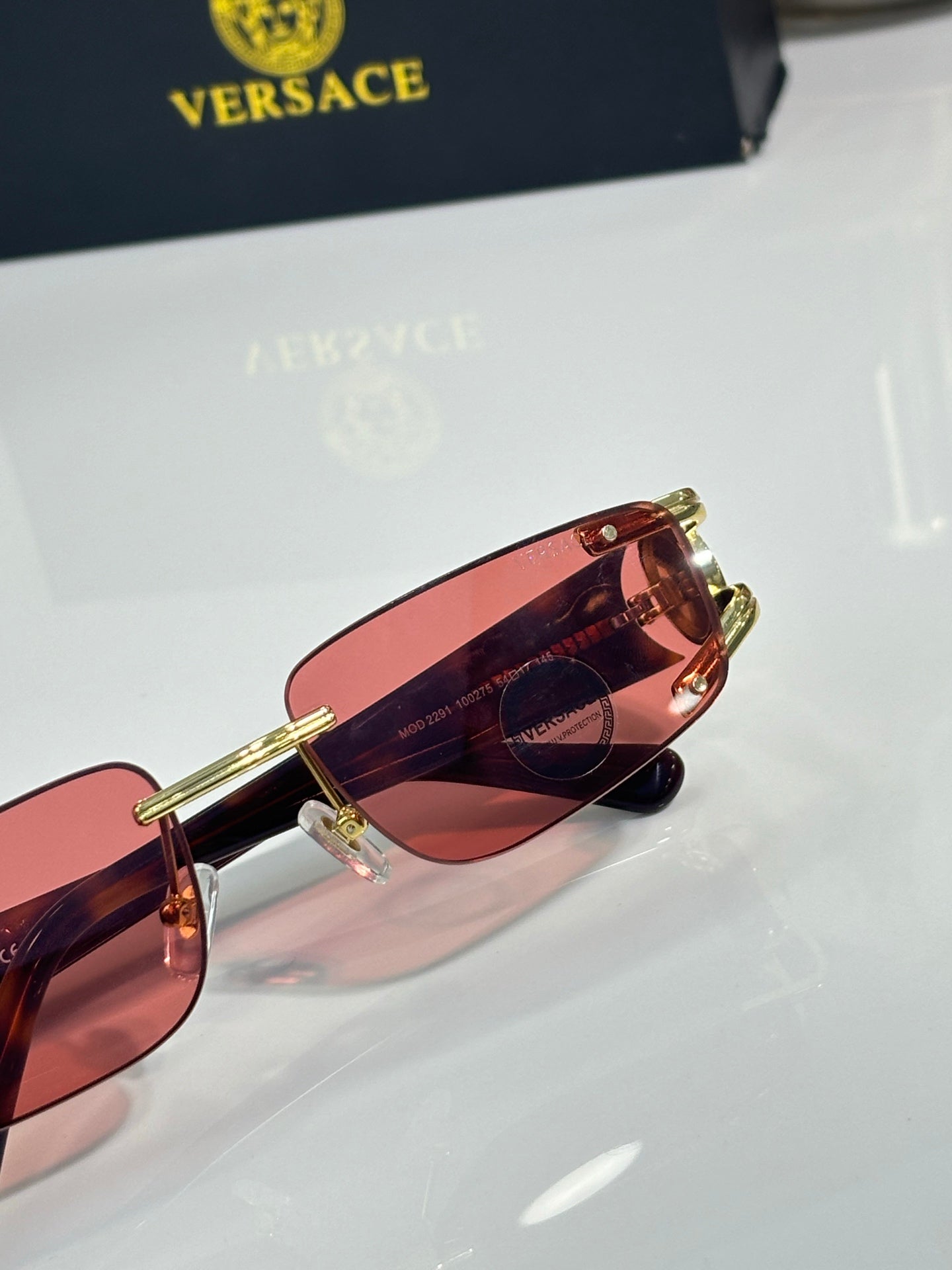 Gold-tone sunglasses close-up with red-pink tinted lens and rim detail