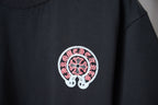 Close-up of dark navy T-shirt chest patch: circular pink flower graphic with white border.