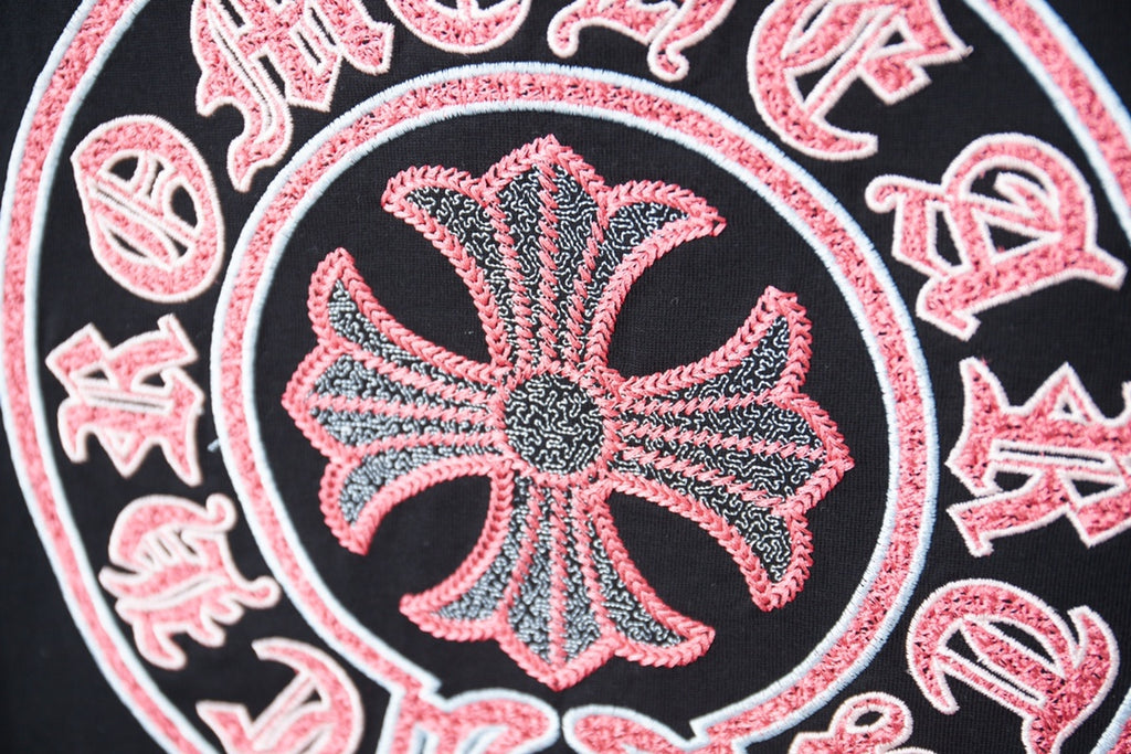 Close-up of pink flower emblem on dark T-shirt with dotted texture and white outline.