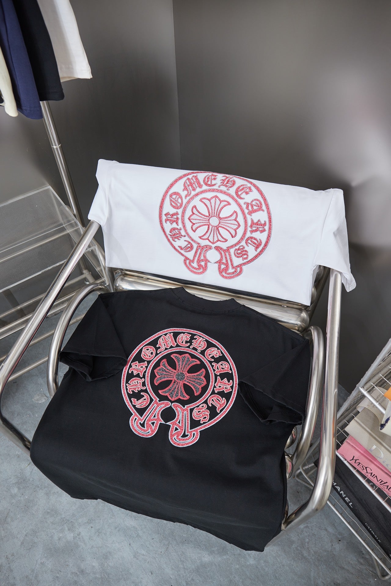 Two short-sleeve T-shirts folded on a chair: white and dark navy with pink circular logo.
