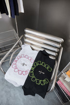 Folded white and dark T-shirts with neon green and pink circular cross graphics