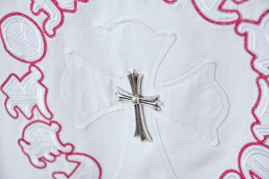 White T-shirt close-up of silver cross embroidery with red ring stitching