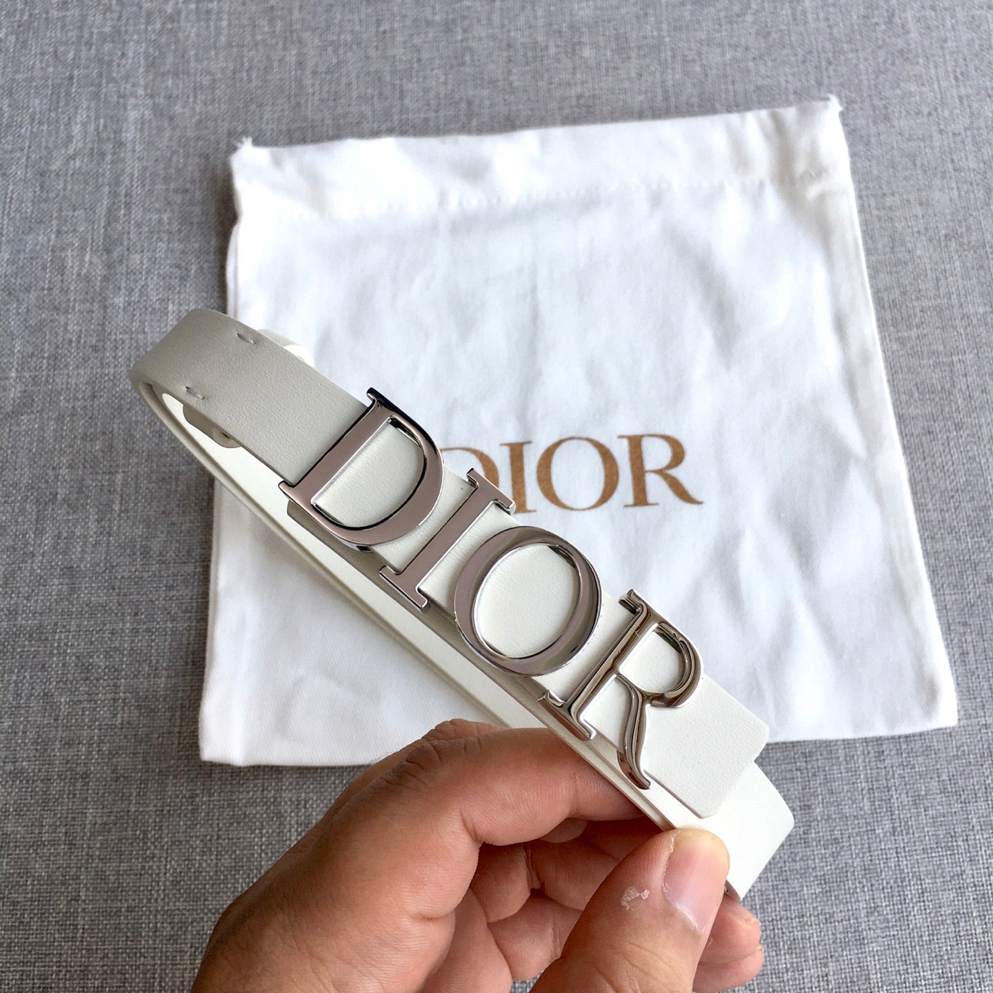 Dior belt held up to show light ivory strap and silver-tone buckle