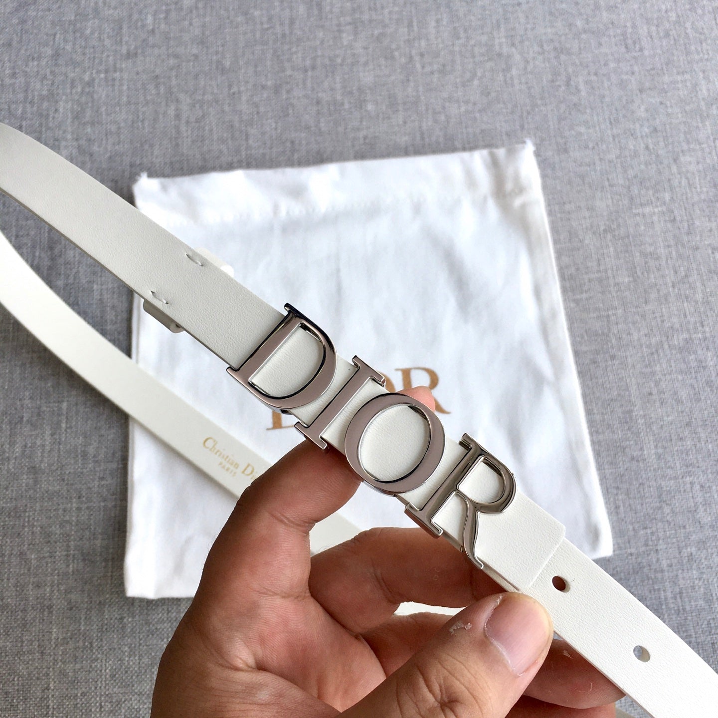 Dior belt with silver-tone buckle detail and light ivory strap, shown in hand