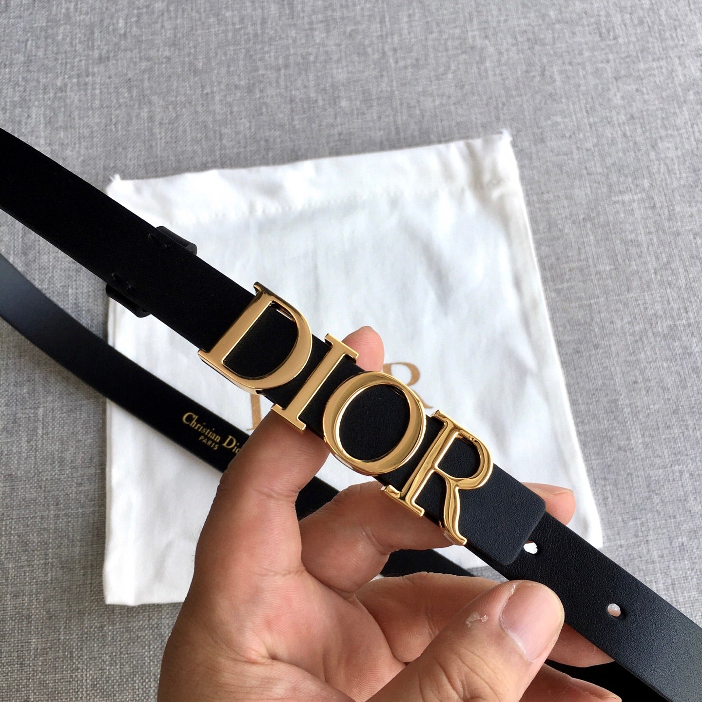 Black leather belt with gold-tone Dior logo buckle, close-up in hand