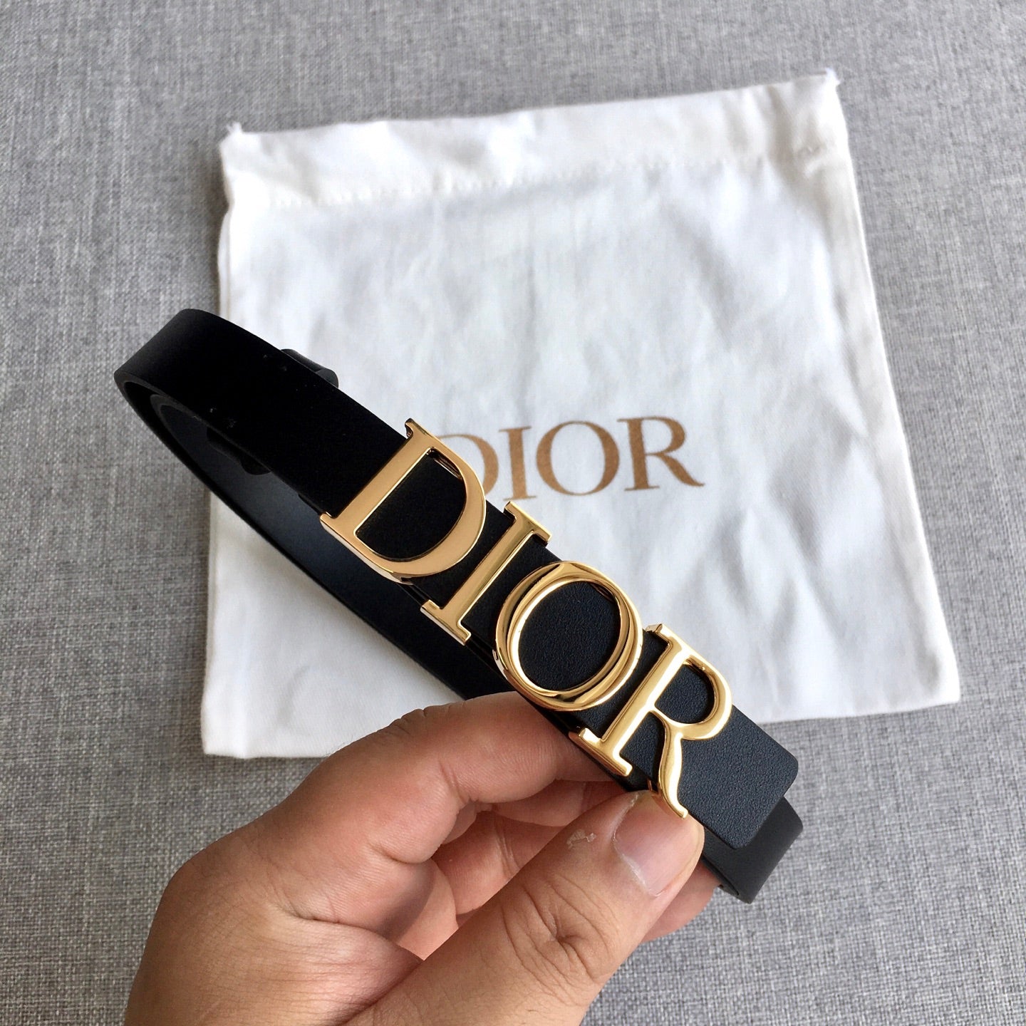 Black leather Dior belt with gold-tone logo buckle, held in hand
