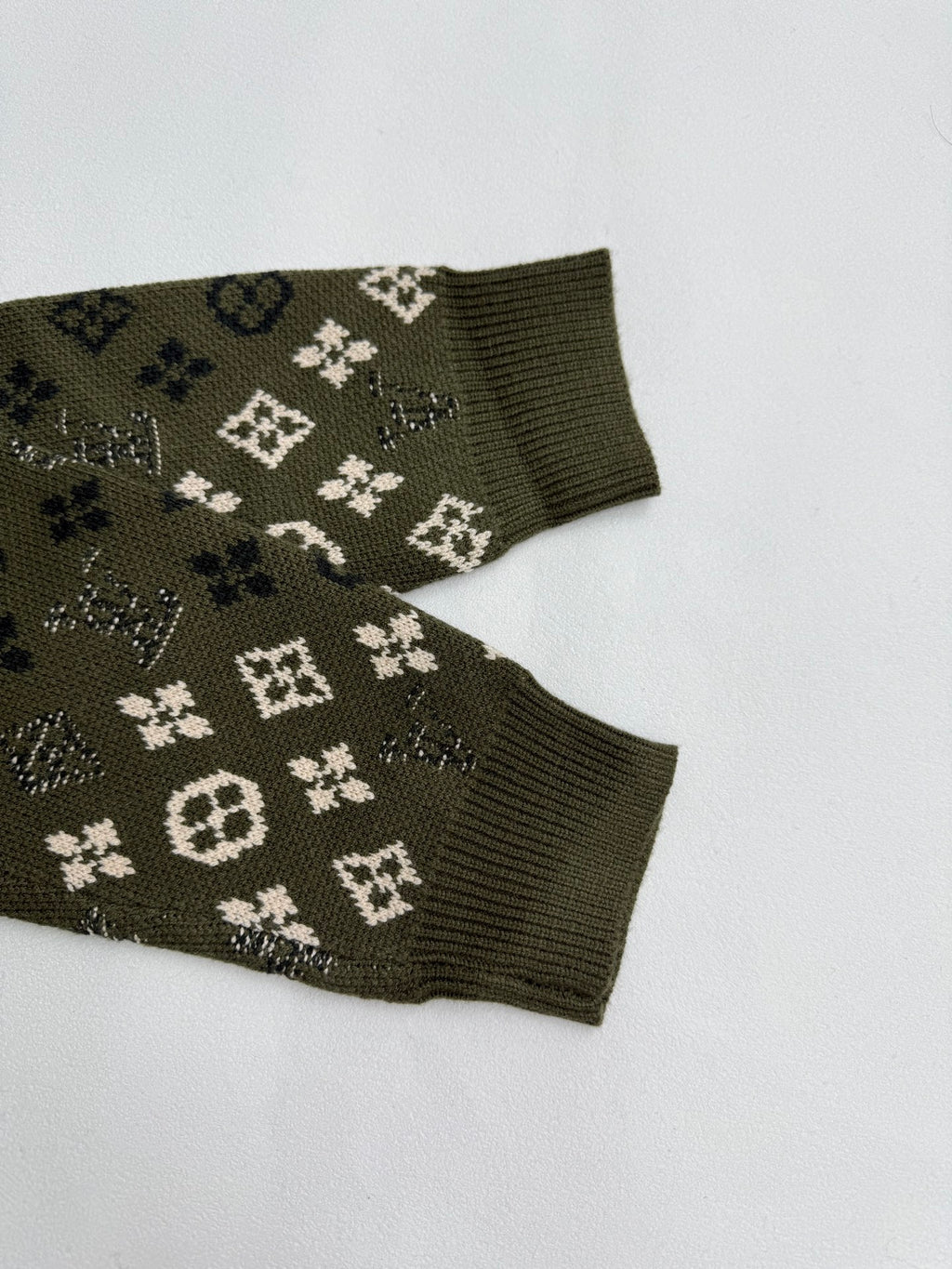 Green knit sweater sleeve cuffs with monogram motifs, ribbed cuffs