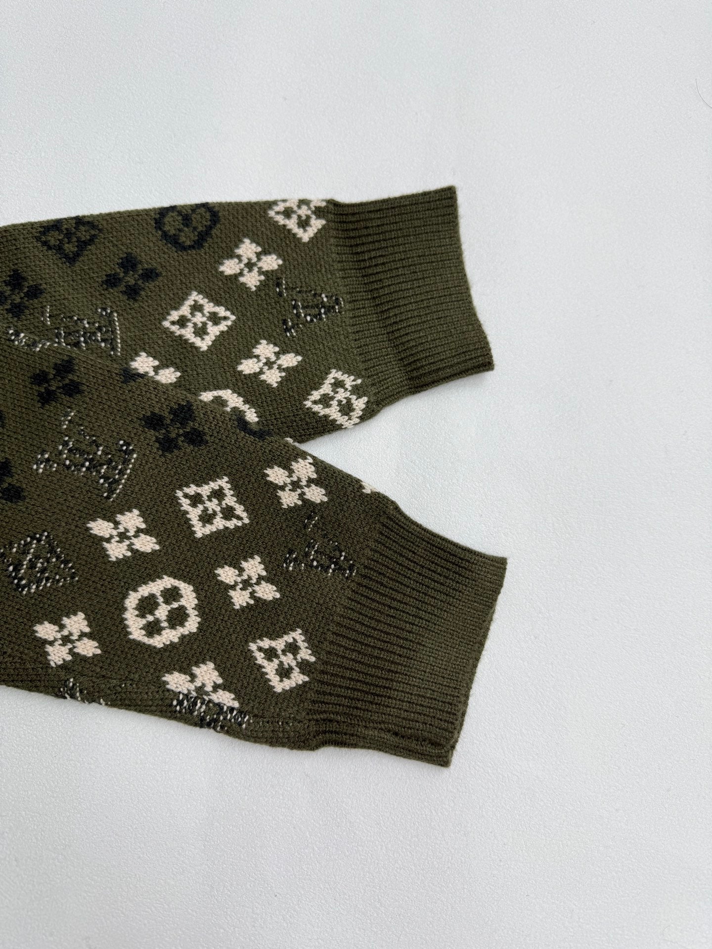 Green knit sweater sleeve cuffs with monogram motifs, ribbed cuffs
