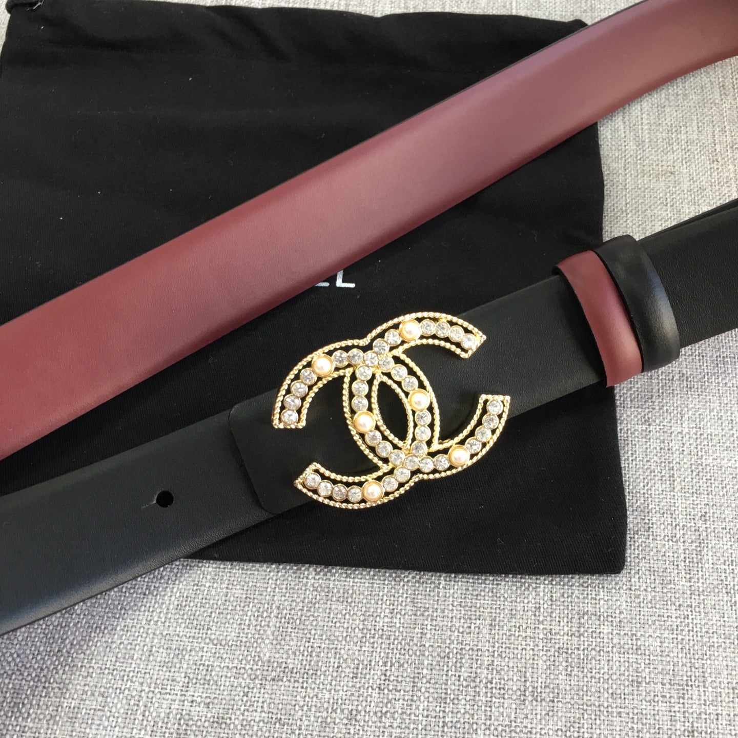 Chanel belt laid flat with black strap, burgundy edge, and gold CC logo buckle