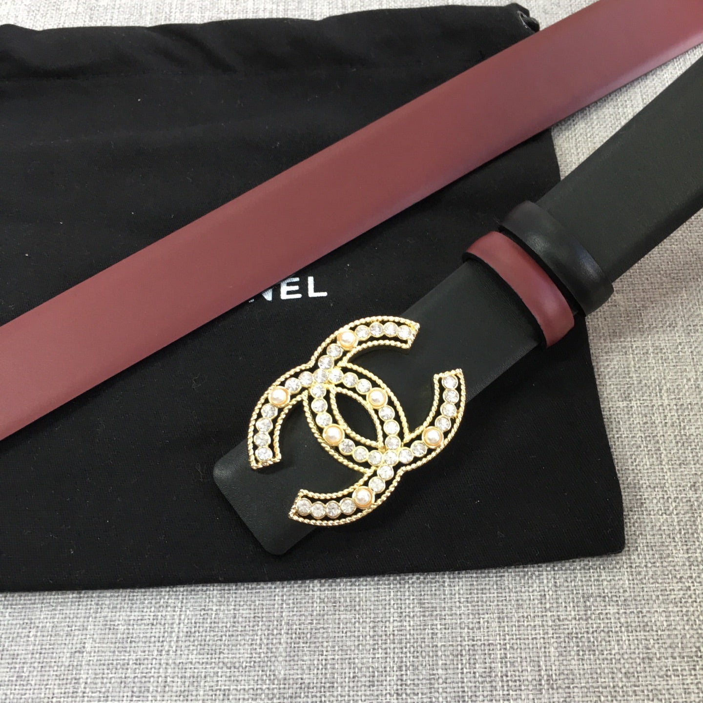 Chanel belt on pouch with black strap, burgundy edge, and gold CC logo buckle