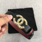 Chanel belt held in hand with black strap, burgundy edge, and gold jeweled CC buckle