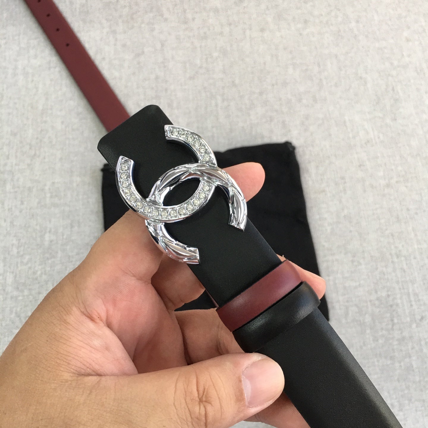 Black Chanel belt with burgundy strap and silver double-C buckle held in hand