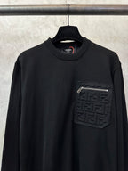 Black long-sleeve sweater with ribbed crew neck and embossed logo chest patch