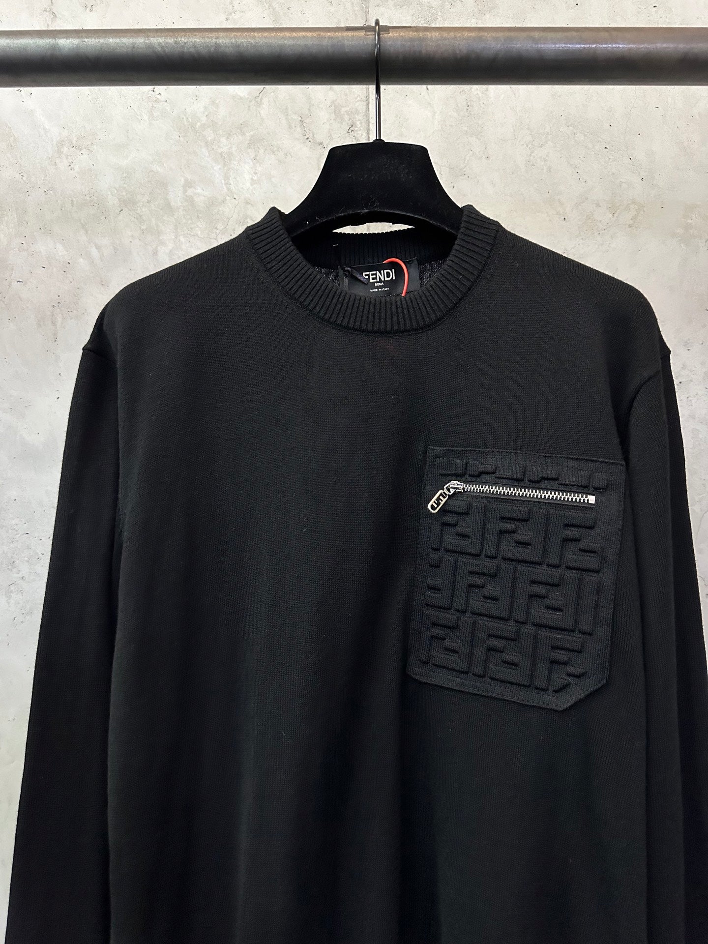 Black long-sleeve sweater with ribbed crew neck and embossed logo chest patch