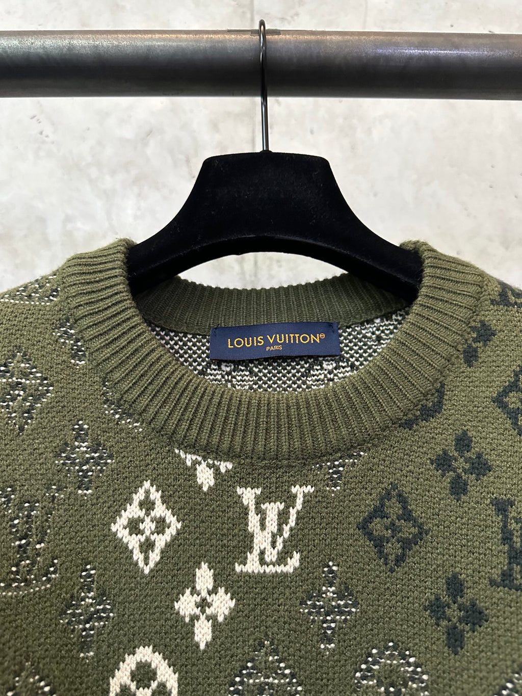Long-sleeve sweater neckline close-up, olive knit with white monogram and ribbed collar