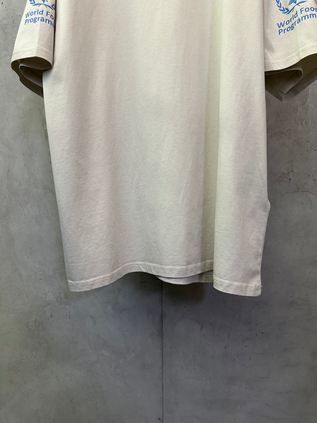 Off-white crewneck T-shirt hem and curved bottom with partial blue sleeve logo