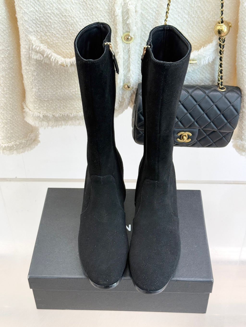 Pair of black suede tall boots with side zippers and block heels, front view on box
