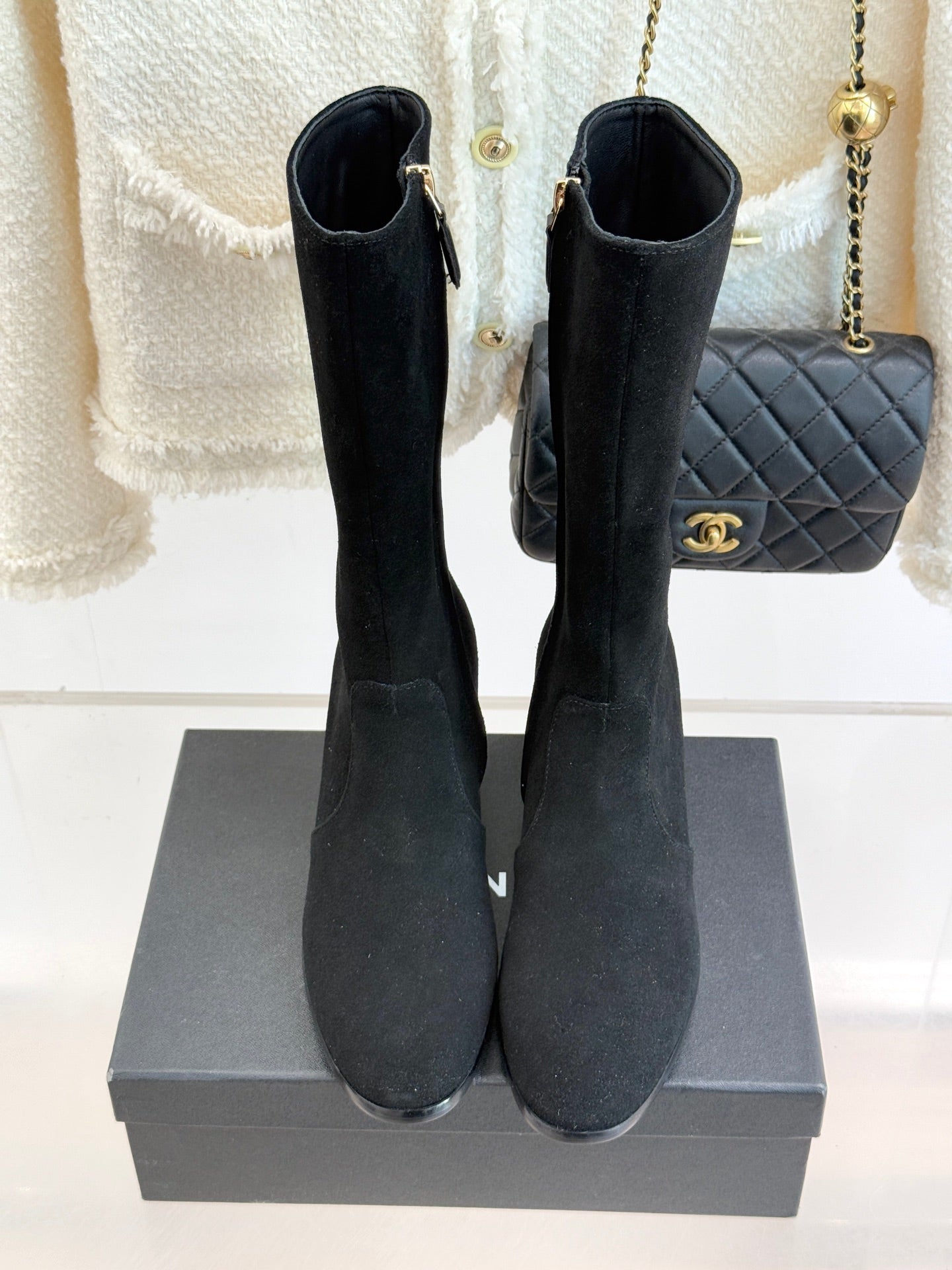 Pair of black suede tall boots with side zippers and block heels, front view on box
