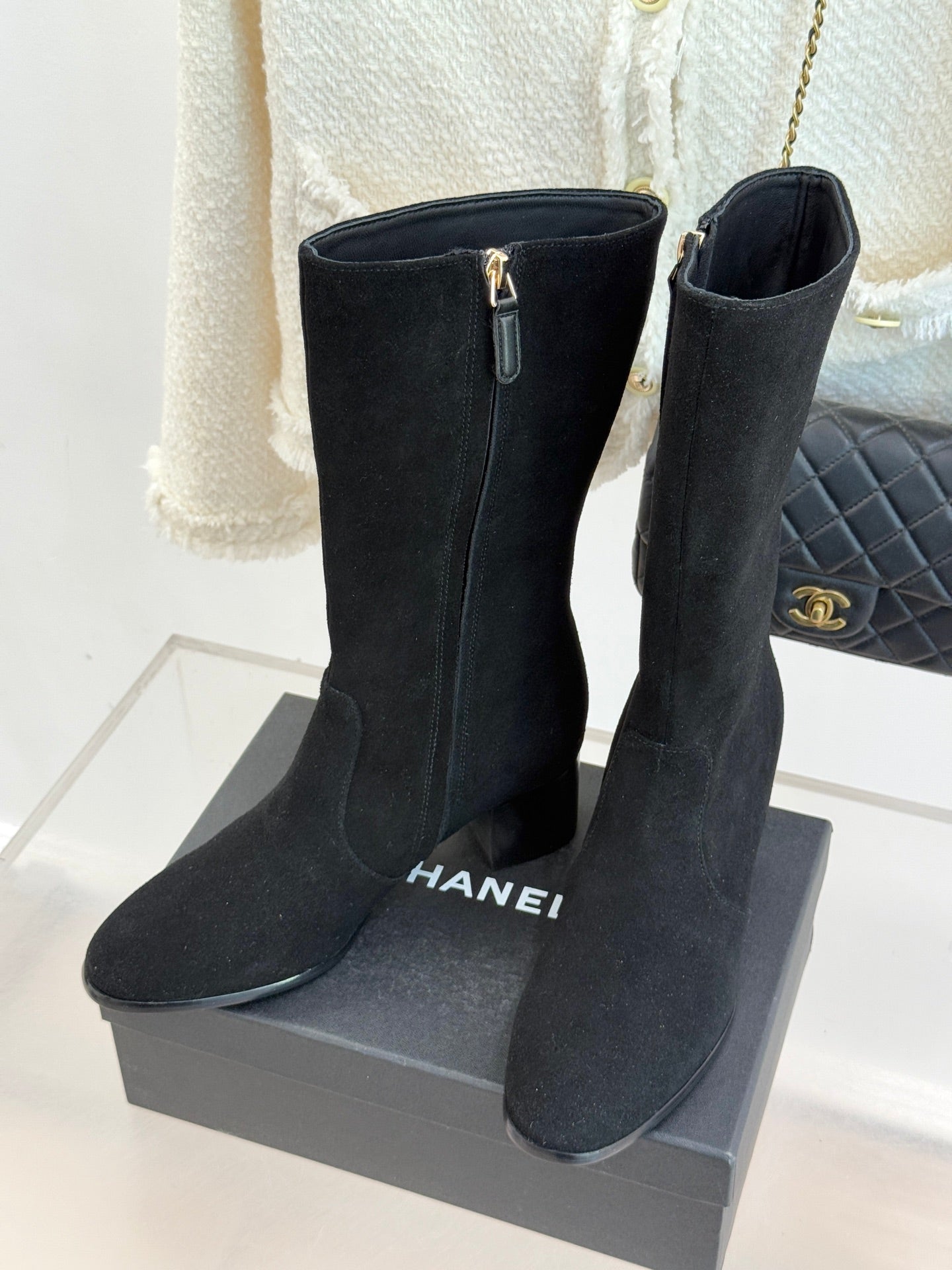 Black suede tall boots with side zippers and block heels, shown upright on box