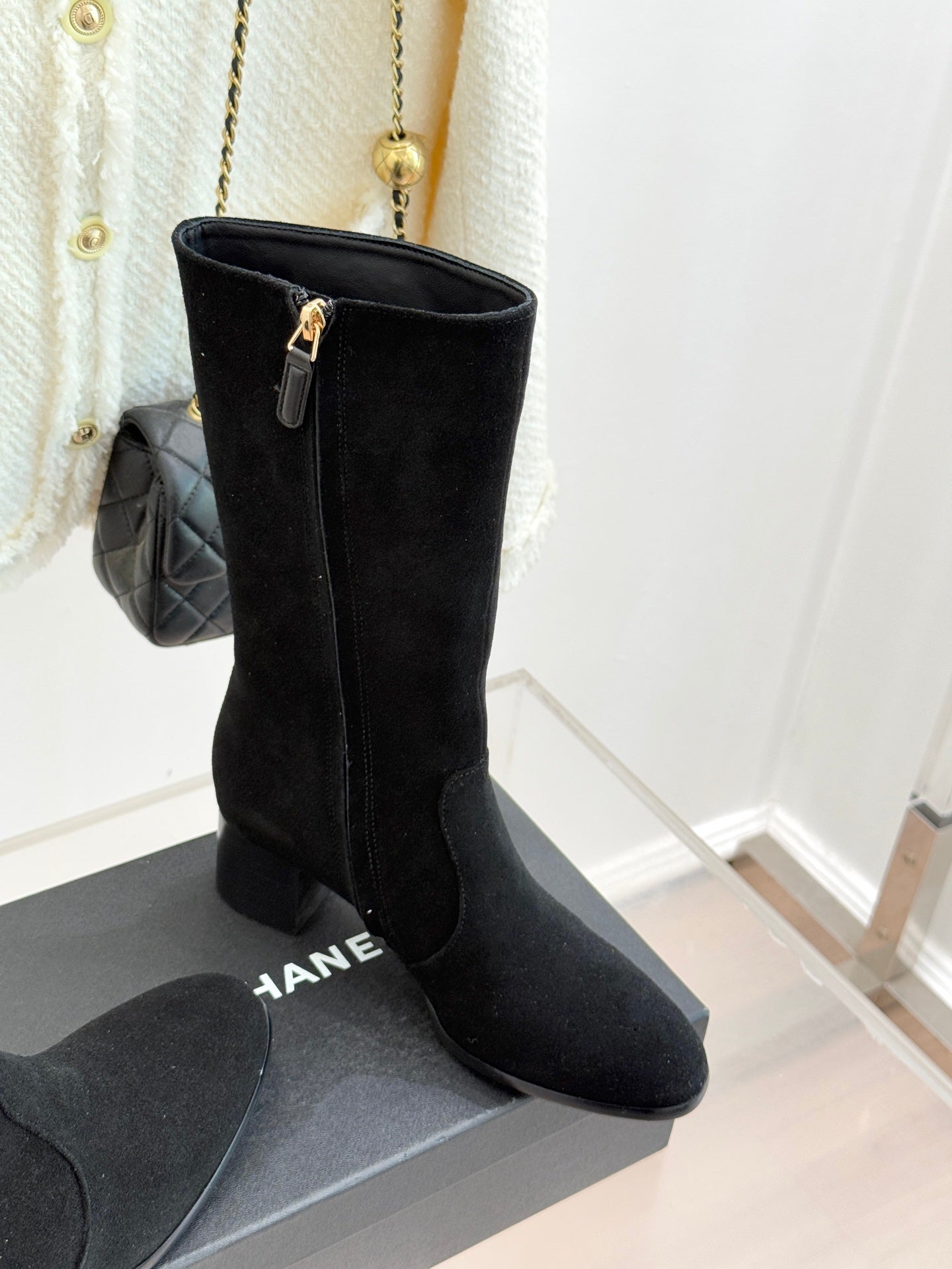 Black suede tall boots with side zipper and block heel, angled view on box