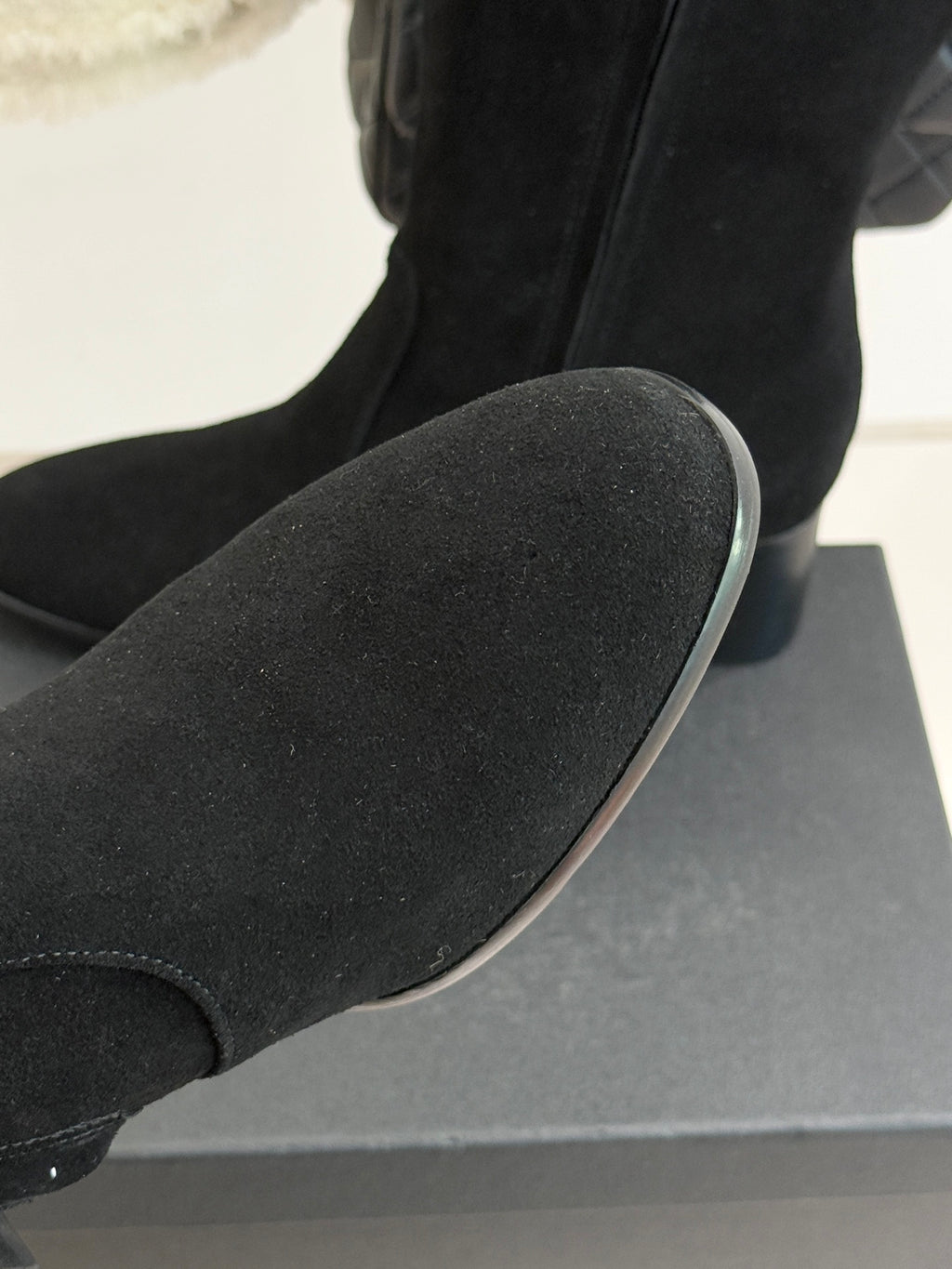 Black suede boot toe and side seam, resting on a display box