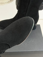 Black suede boot toe and side seam, resting on a display box