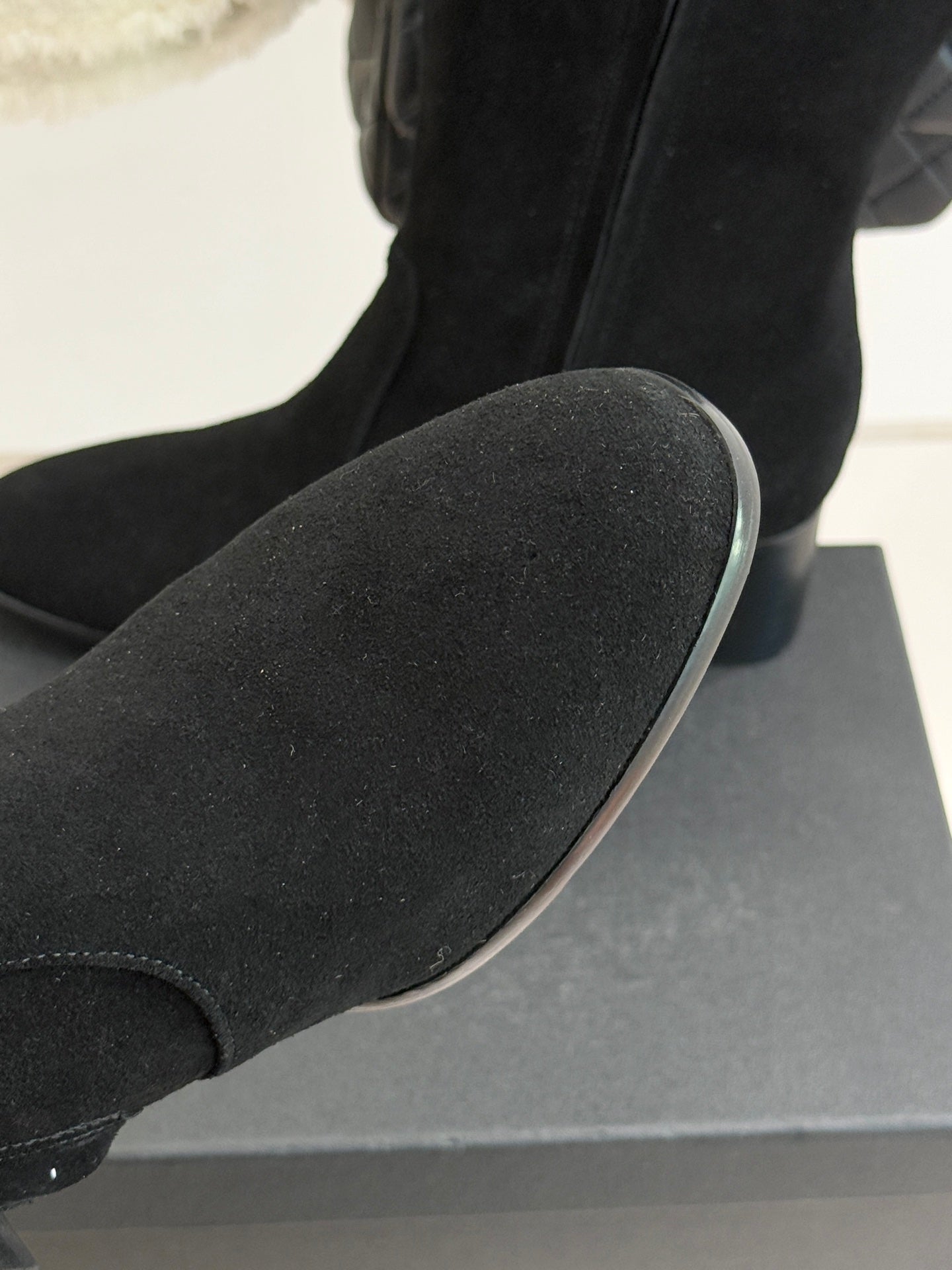 Black suede boot toe and side seam, resting on a display box