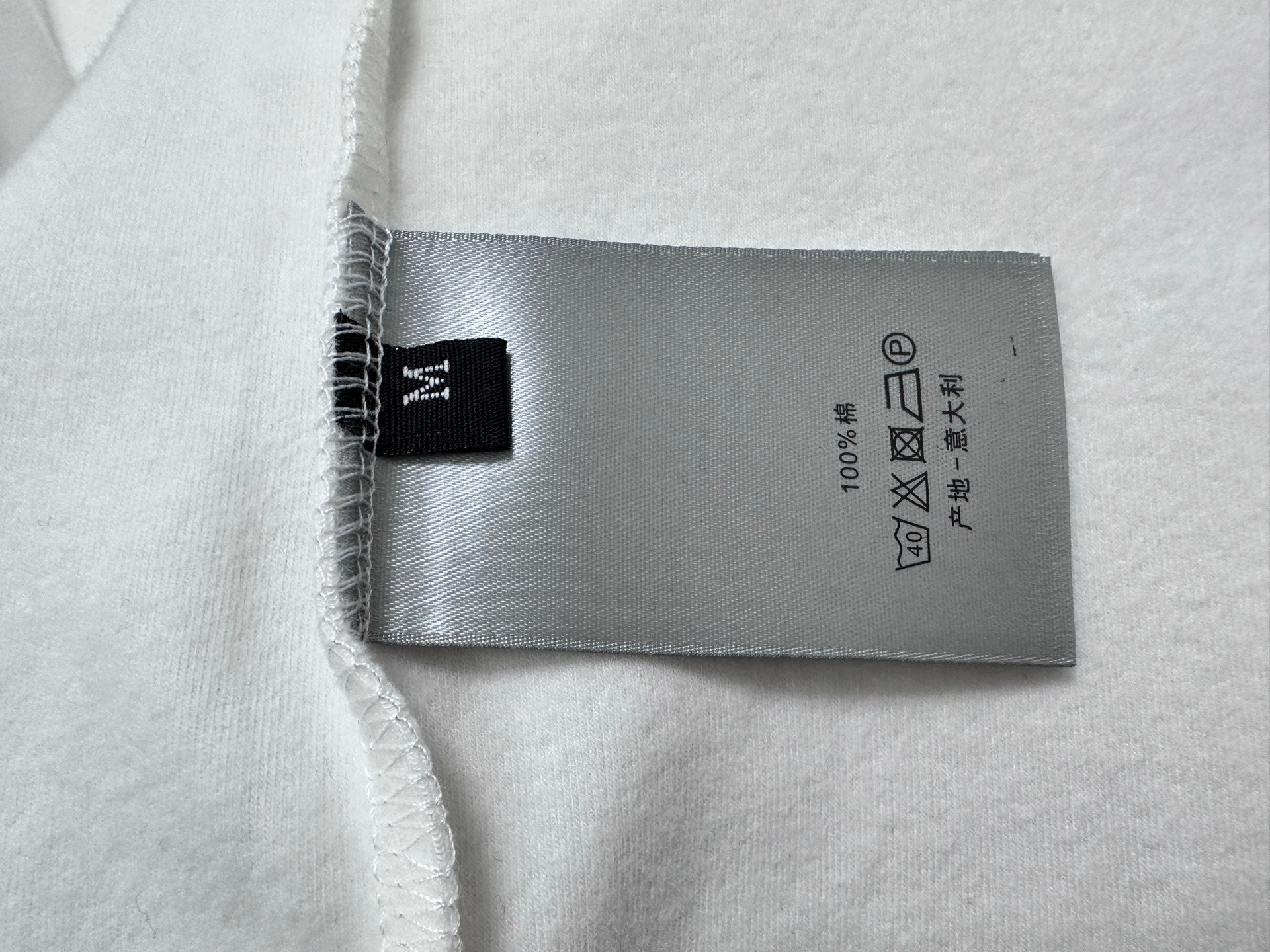 White top with gray fabric care label and black brand tag at hem