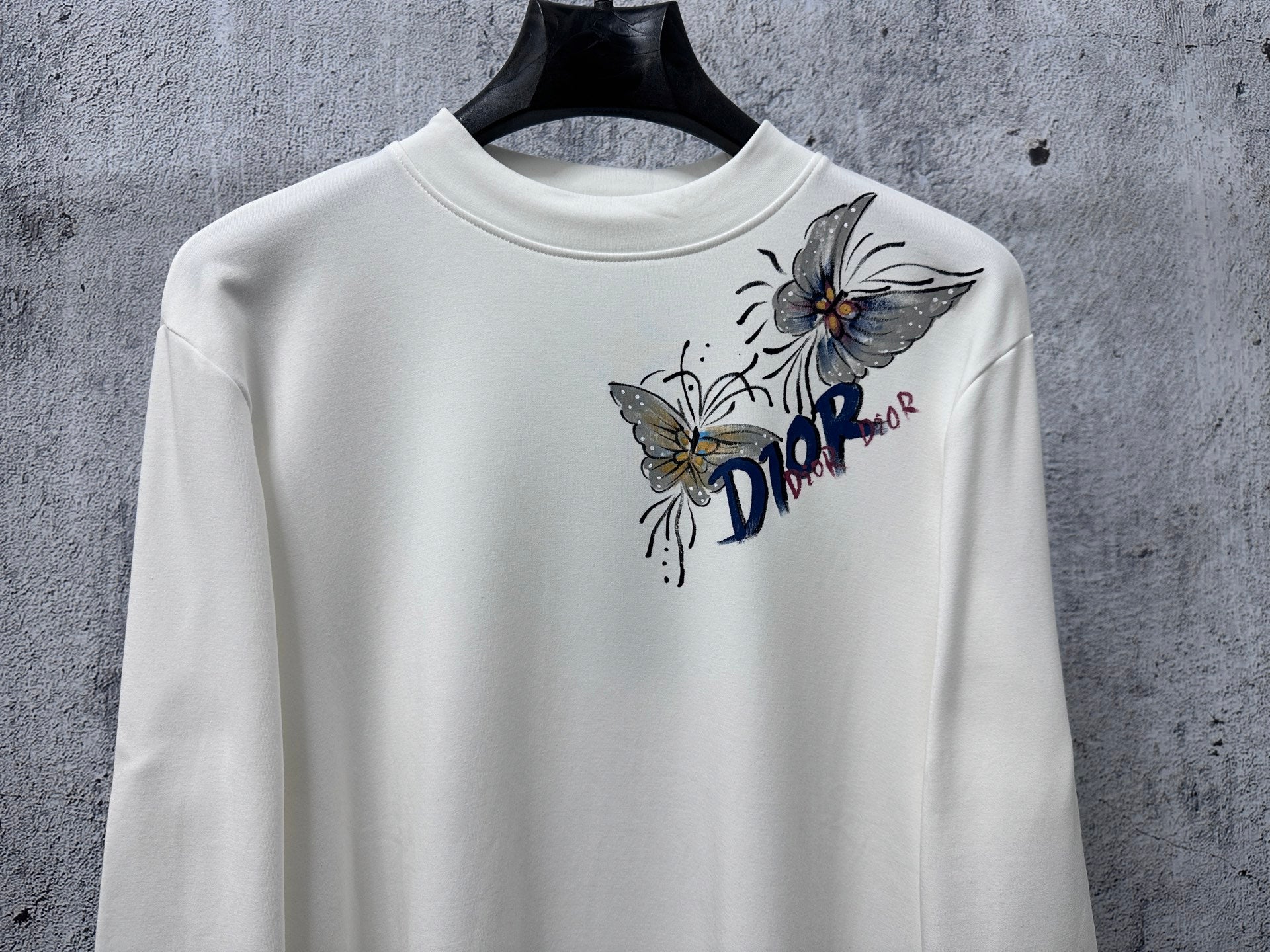 White long-sleeve crew-neck top with Dior floral and butterfly graphic.