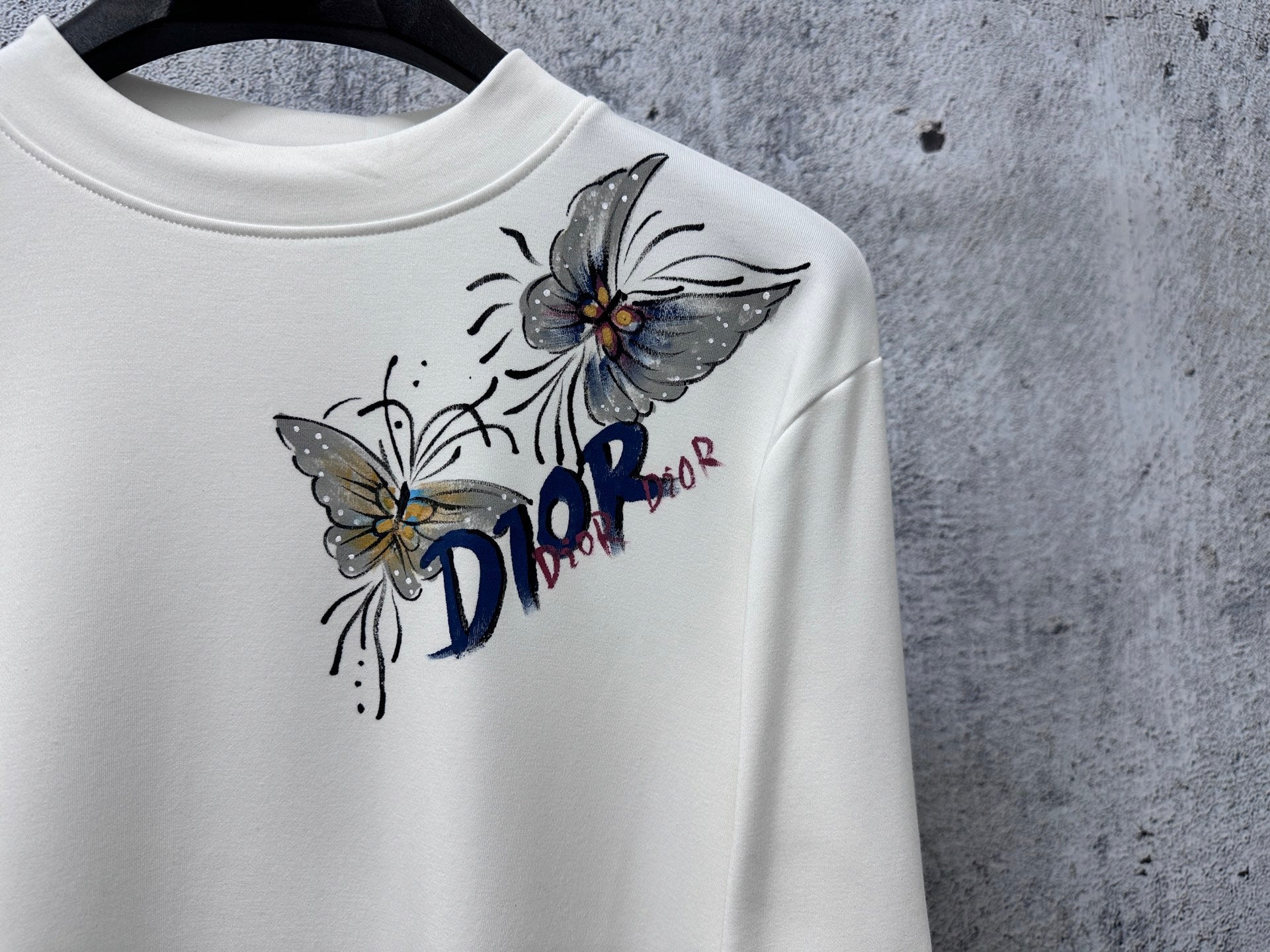 White long-sleeve top with Dior flower and butterfly graphic, crew neckline.