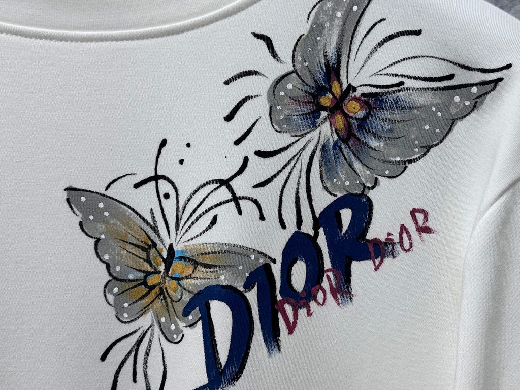 White long-sleeve top with blue Dior butterfly and flower graphic detail.